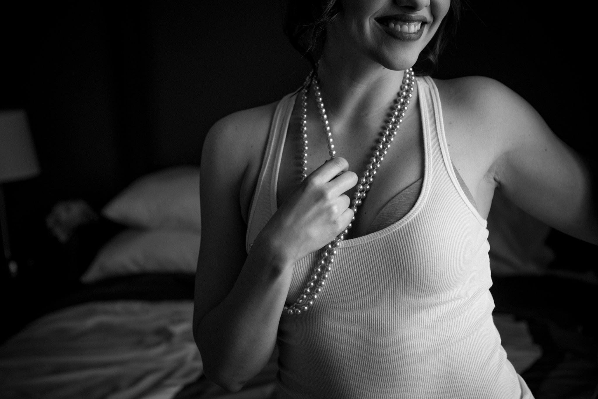 woman plays with pearl necklace during regina boudoir photography session black and white photograph