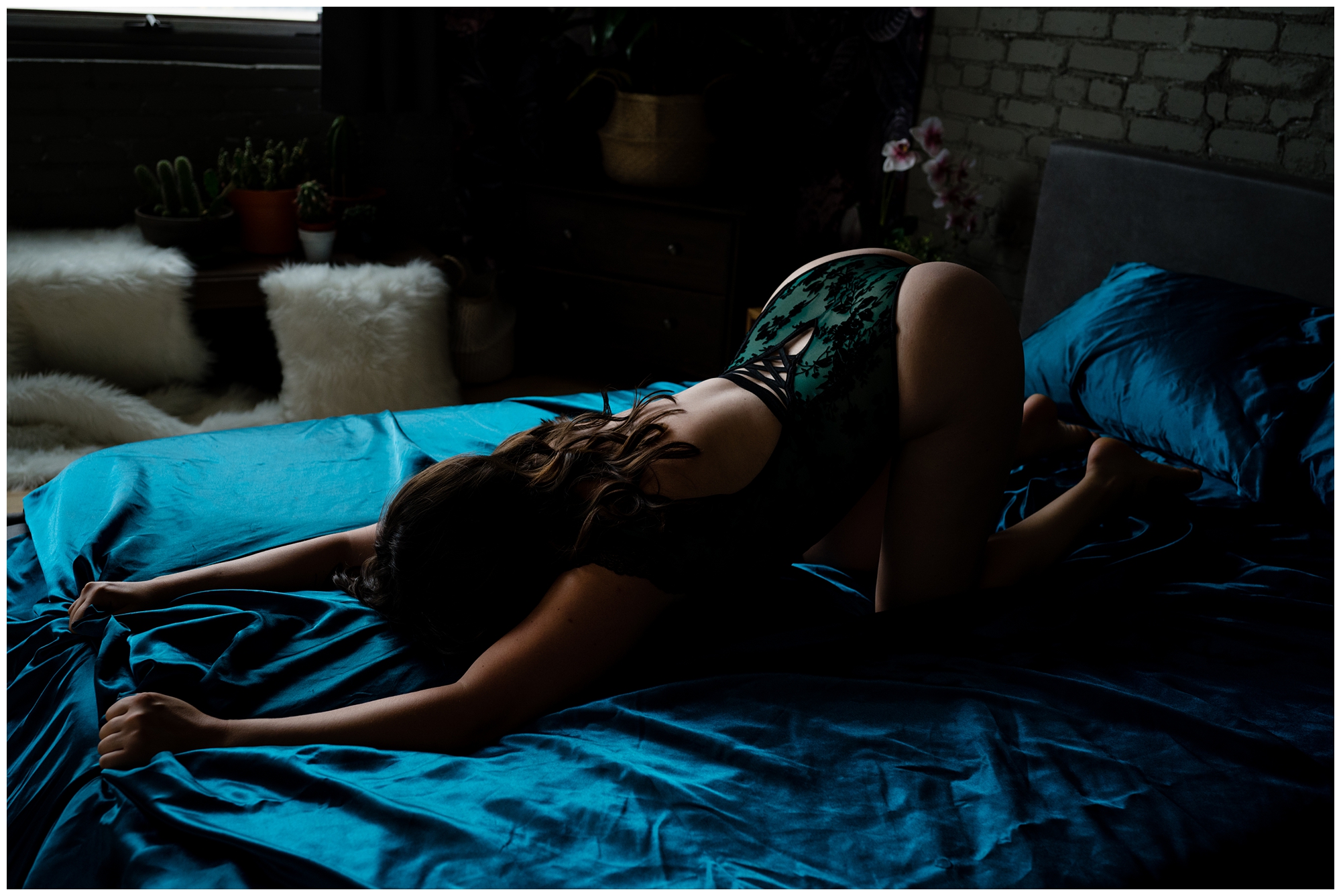 image of a woman face down on a bed covered in blue satin sheets during her nelson bc boudoir session