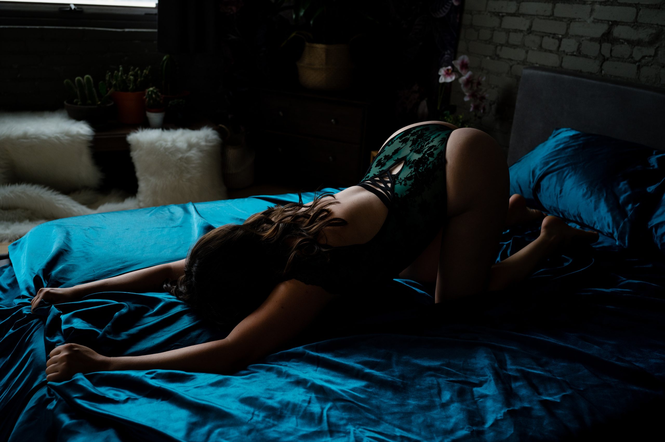 photograph of a woman in a boudoir session she is wearing an emerald green lingerie set and is face down on the bed