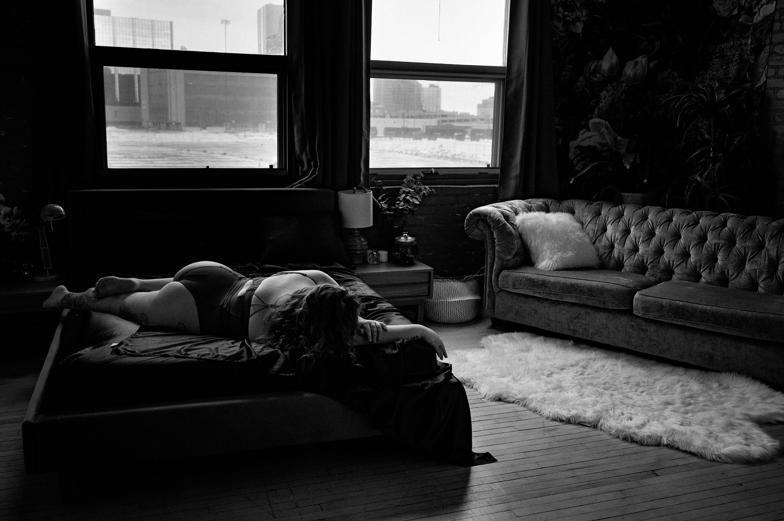 a woman lays on a bed diagonally and is backlit by the two bright windows