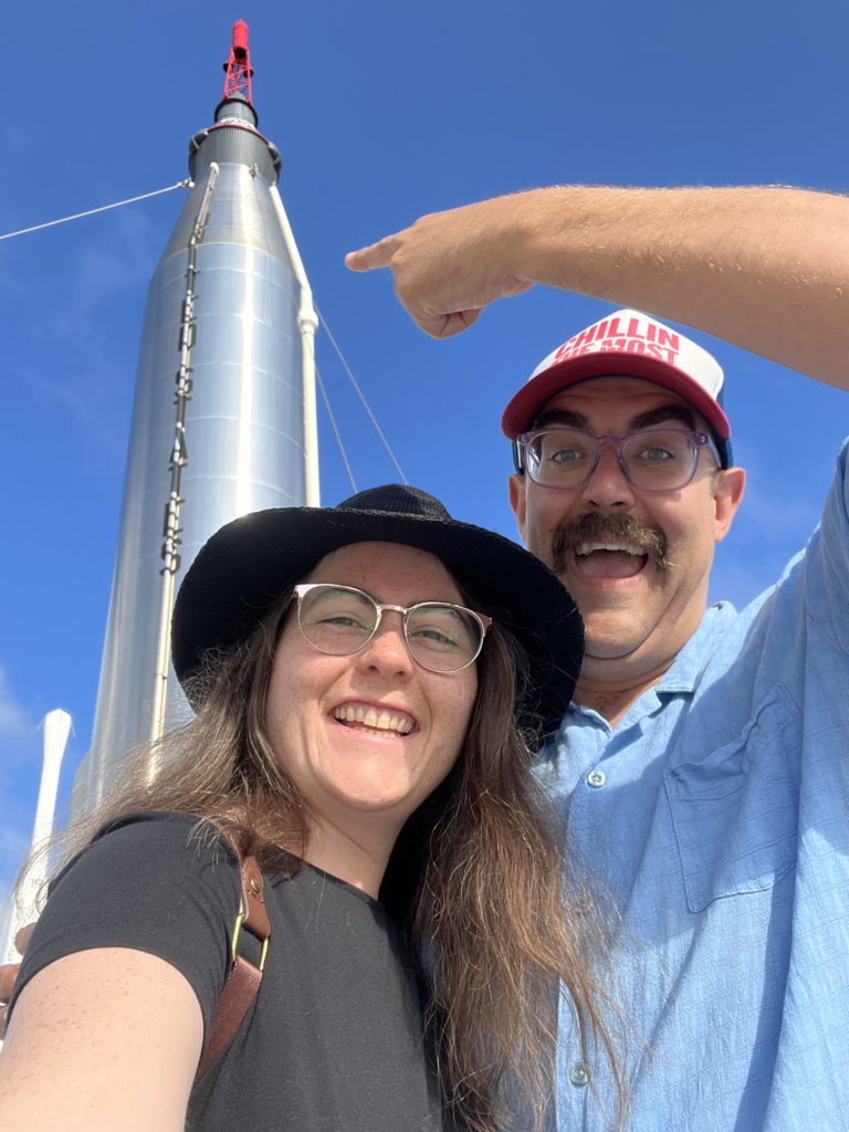 erika and her husband shawn standing in front of a rocket ship at the kennedy space centre in florida