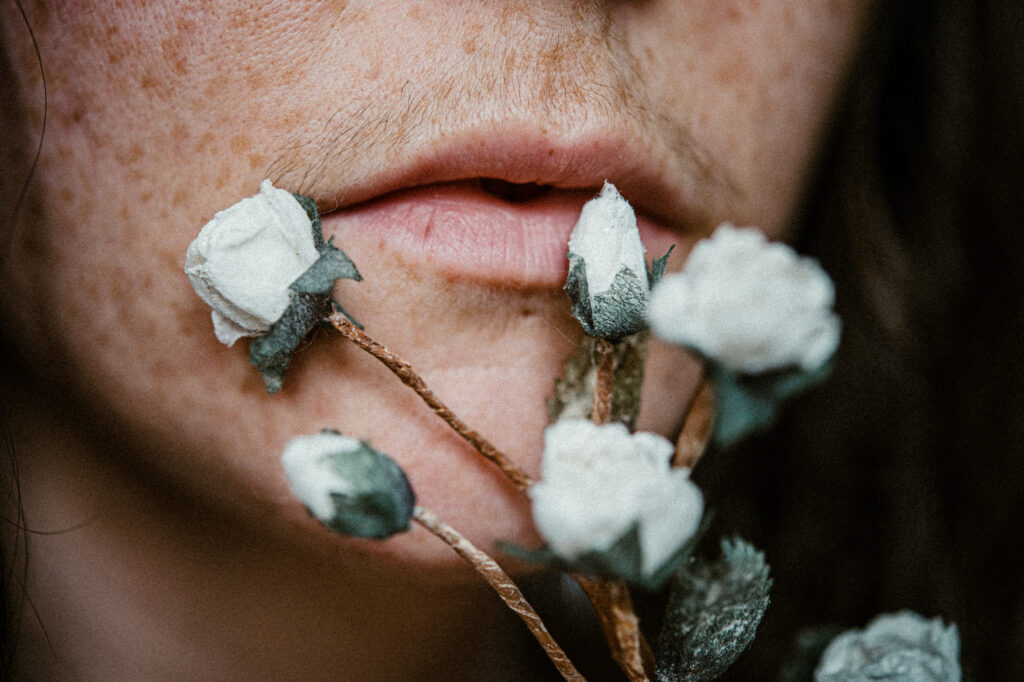 a freckle face woman holds up small white silk flowers against her lips